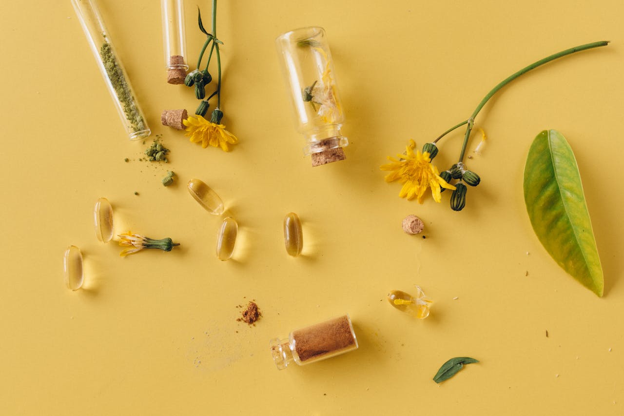 services-02 A flat lay of glass bottles, capsules, and flowers on a vibrant yellow surface, representing natural remedies.